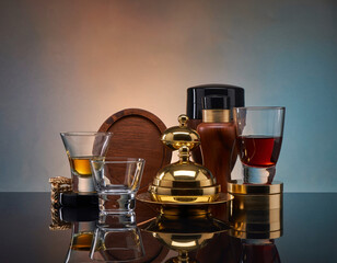 Elegant glassware and golden accents arranged on reflective surface create a sophisticated and luxurious still life with warm and cool lighting, evoking opulence and refinement.