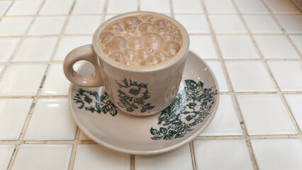 A glass of traditional teh tarik (pulled tea) with a distinctive layer of foam, served at a restaurant table in the evening. This warm beverage is popular in Southeast Asian eateries.