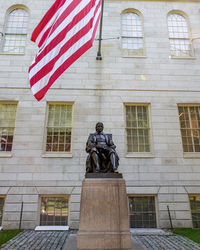 John Harvard statue underneath US flag, in front of University Hall in Old Harvard Yard, Harvard University, Cambridge, Massachusetts MA, USA	