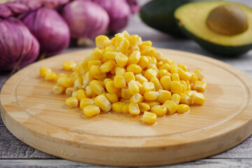 Fresh corn piled on a wooden board with vegetables nearby