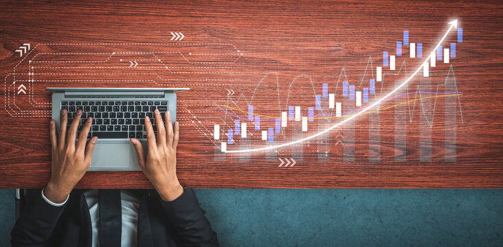 A top-down view of a person hands on a laptop, illustrating financial growth through stock market data visualization on a wooden table. Impute
