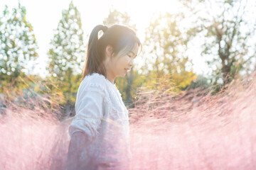 A Young Woman Standing in Pink Grass Under the Sunlight