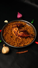 Roasted Chicken Leg on Spiced Rice in Metal Dish with Garlic and Chili Peppers on Black Surface