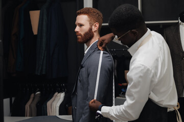Professional tailor measuring customer for bespoke suit in luxury designer atelier