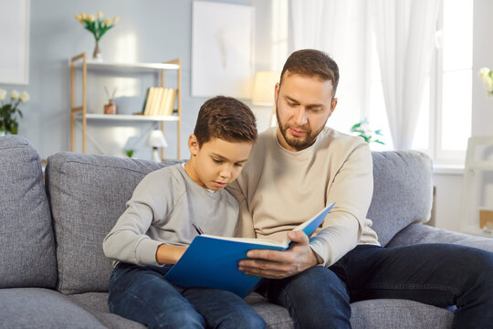 Father is engaged in raising his little son and helping him complete exercises from notebook. Preschool boy, appearing determined, writes intently while his dad provides guidance and encouragement. - Powered by Adobe