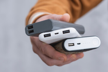 Close-up of a person holding several portable power banks in hand. Modern charging technology, multiple USB ports and battery indicators for energy on the go.