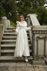Fototapeta premium full length portrait of beautiful blonde female model wearing historical white gothic wedding gown, walking down staircase of romantic fairytale castle location with stone balconies