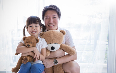 Happy father young toddler daughter holding teddy bears posing playfully in a bright room natural light and curtains. Father’s day