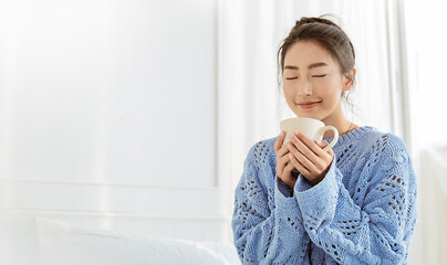 Portrait of young beautiful asian woman relax face hand holding mug of coffee in winter bedroom....