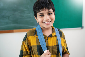 Portrait of cheerful young student wearing yellow checkered shirt and backpack straps, smile confidently in front of chalkboard at school. Back to school education