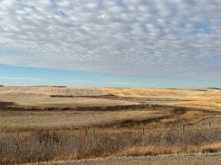 Fototapeta premium Rural Alberta landscape beneath a textured sky filled with rolling clouds, overlooking expansive brown fields and distant ridges. Captured on a calm day