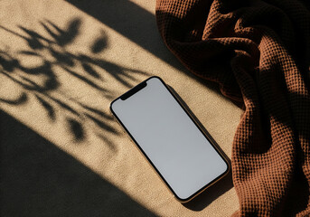 Top View of Smartphone with Blank Screen on Textured Surface with Brown Cloth and Shadow of Plant Casting Soft Lighting
