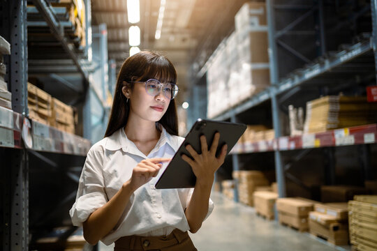 A woman wearing glasses is using a tablet in a warehouse