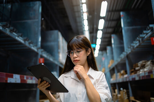 A woman wearing glasses is looking at a tablet in a warehouse
