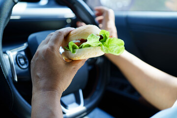 Asian woman driver hold and eat hamburger food in car.