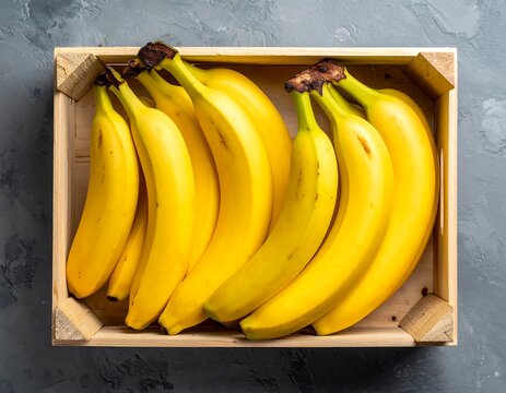 Bright yellow bananas packed tightly in a rustic wooden crate on a gray background