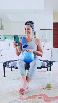Fit mature woman checking smartphone after home workout