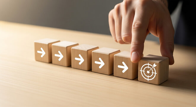 Business hand arranging wooden blocks with arrows and target icon representing strategy direction and goal achievement
