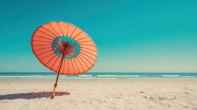 Retro style orange parasol standing on a sandy beach with gentle waves and clear blue sky in the background during a sunny day