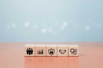 Wooden cubes with business and teamwork icons including growth chart, security shield, handshake, and gears on pastel background, symbolizing collaboration, success, and strategy.