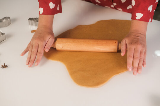 Close up of a young woman's hands in red pajamas with hearts rolling out gingerbread dough with a rolling pin. Making gingerbread for Christmas.