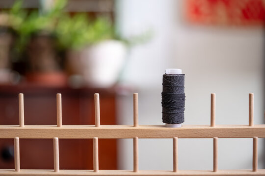 un carrete de hilo el&aacute;stico sobre porta hilos de madera con fondo desenfocado con plantas