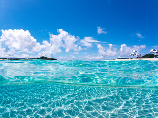 比島の白砂ビーチの半水面撮影。沖縄特有のサバニ（双胴船）、観光客やパラソル、テントが見える。美しいサンゴ礁と熱帯魚の群れ。 安室島沖縄県 島尻郡慶良間諸島座間味島-2025 サンゴの産卵があり卵が漂う。沖縄本島から40km西方の諸島。30以上の島嶼群全体が国立公園に指定。珊瑚礁の青い海と白い砂浜は世界屈指の美。貴重な動植物が多数生息。