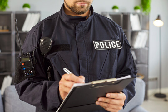 Fototapeta Close-up male police officer dressed in uniform stands indoors writing accident or criminal details on clipboard during official investigation or patrol. Legal procedures, security service concept 