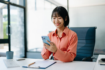 Confident Asian woman with a smile standing holding notepad and tablet at the modern office.