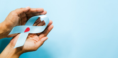 World diabetes day and blue ribbon awareness with red blood drop in woman hands isolated on a blue background. World diabetes day,14 november. Copy space. Top view