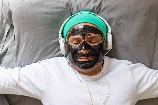 Latin man with headphones and face mask resting on his bed