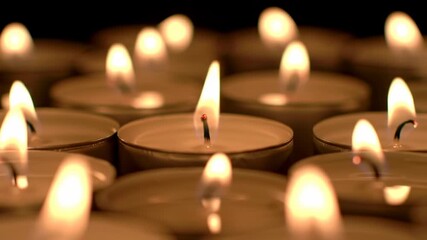 Close-up of multiple lit tea light candles arranged on a black background, creating warm ambiance and soft glow