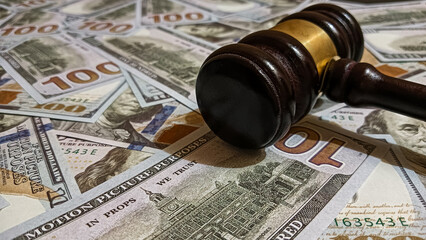 Wooden judge gavel placed on a pile of hundred-dollar bills representing law, justice, corruption, and financial judgment in legal or business contexts.