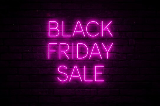 Vibrant pink neon sign reads black friday sale illuminated against a dark brick wall background