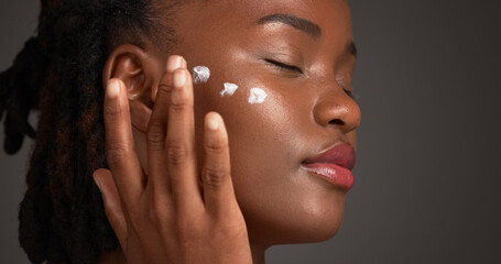 Black woman, studio and skincare with lotion for moisturizer or face cream on a gray background....