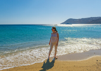 Mujer a contraluz de vacaciones por la playa Elia de la isla de Mykonos. Estilo de vida alegre y de...