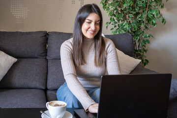 Woman smiling while typing on laptop during remote work on home couch with copy space