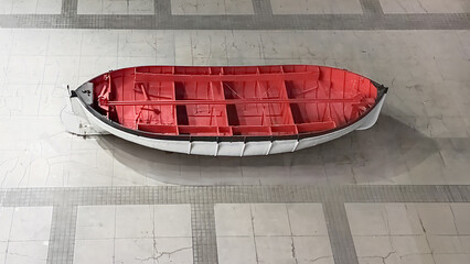 Vintage red and white lifeboat boat empty on tiled floor background, aerial top view of nautical rescue vessel, old maritime safety transportation equipment display