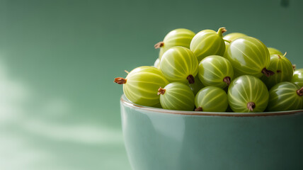 A bowl filled with fresh green gooseberries against a soft green background
