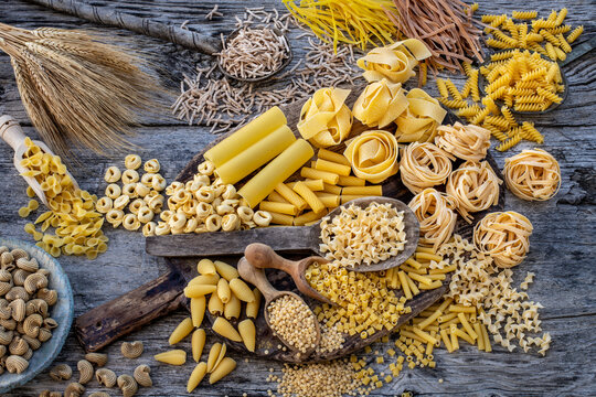 Different types of Italian pasta on rustic wooden table, in the spoons, cutting board and bowls