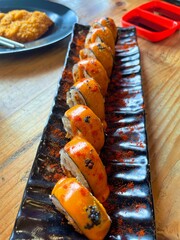 Fresh sushi rolls with spicy orange sauce served on black plate. A modern Japanese cuisine presentation symbolizing luxury, flavor, and the art of traditional culinary craftsmanship.