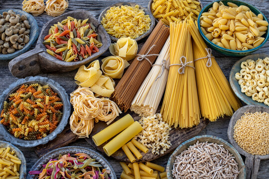 Different types of Italian pasta on rustic wooden table, in the spoons, cutting board and bowls 