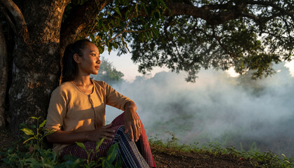 Woman sitting under a tree with mist in the background.