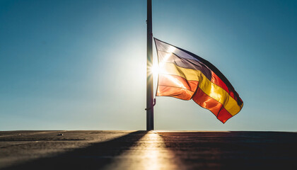 A colorful flag flies on a pole against a bright blue sky.