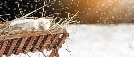 Manger with baby Jesus and hay on snow against dark background