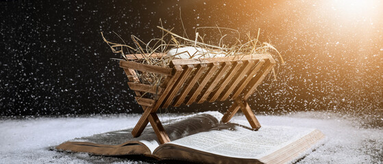 Bible and wooden manger with dummy of baby on black background. Concept of Christmas story
