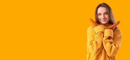 Beautiful young woman in stylish sweater and mittens on yellow background with space for text