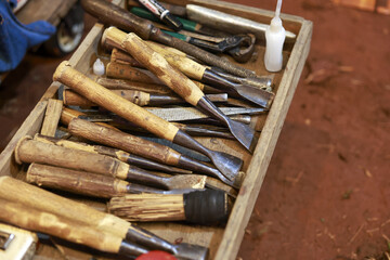 Rustic collection of woodworking tool, chisel, and gouge with bamboo handle in wooden box at workshop. This messy arrangement evokes sense of authentic craft and labor