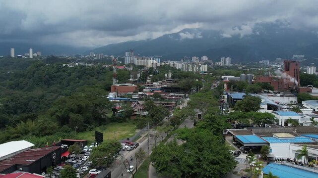A cinematic drone shot capturing the city of Ibague on the horizon as the drone pulls back over the lush vegetation of Mirolindo roundabout.