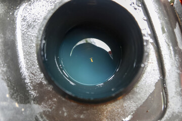 Mysterious close up showing dark blue liquid inside circular metal drain. tiny golden fleck floats on surface, creating point of interest and reflection
